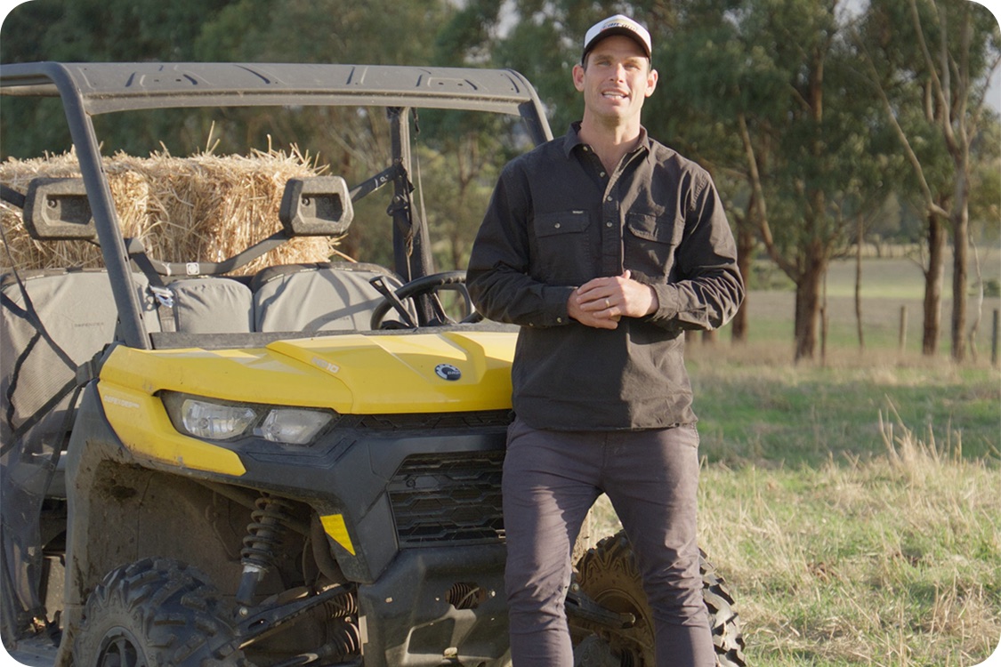 Tom Hawkins leaning on a Can-Am Defender beside hay bales